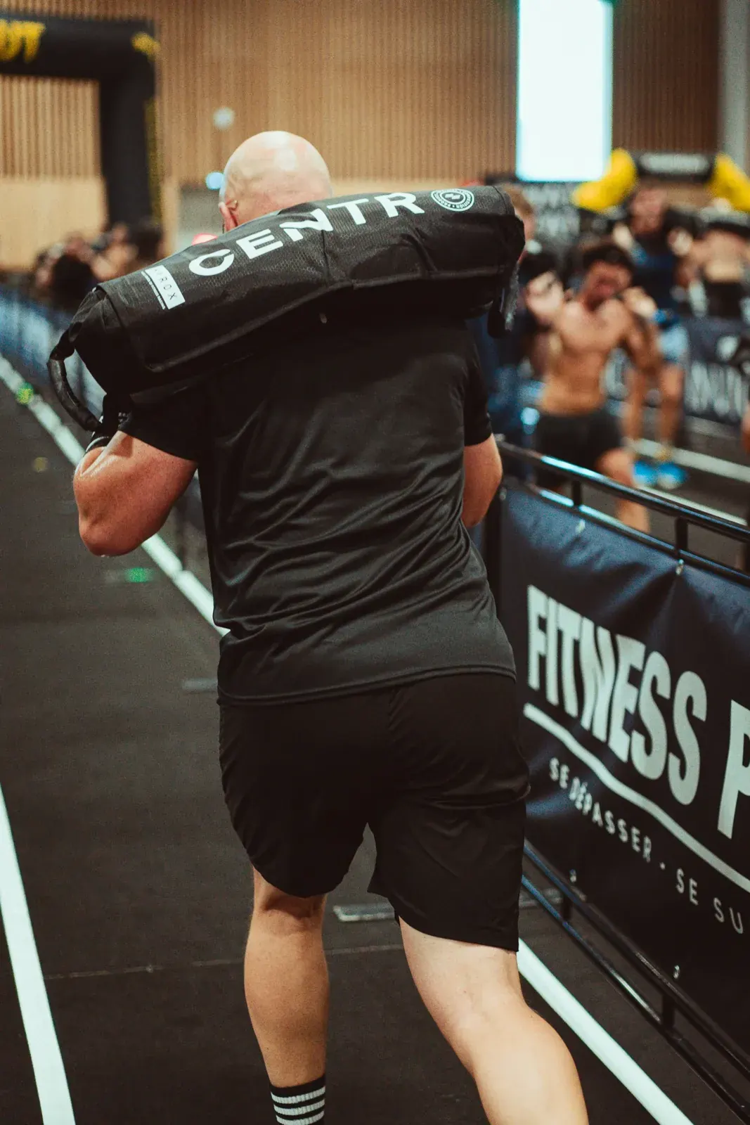 Athlète de dos aux Sandbag Lunges, devant les banderoles Fitness Park, à Hyrox Paris